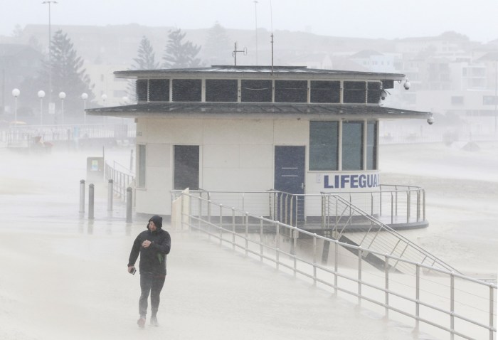 A man struggles against the strong winds as he walks along the Bondi Beach promenade.