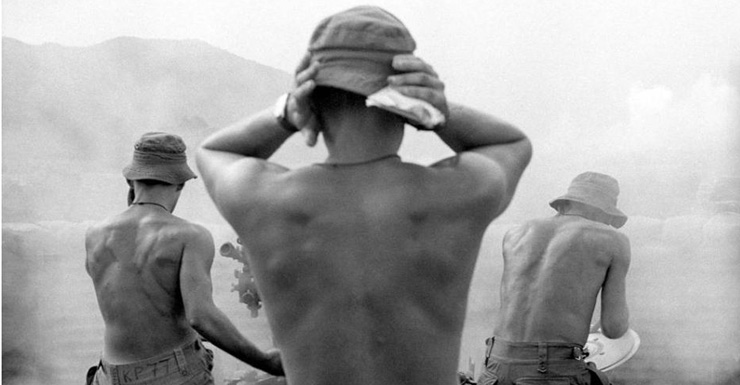 Soldiers cover their ears as they fire a large weapon during the Vietnam War.