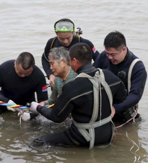A woman is helped after being pulled out by divers from a sunken ship cabin.