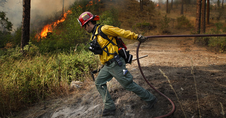 Snohomish County Fire District 7 firefighter Brandon Gardner pulls a water hose into position while helping prevent a wildfire from spreading to a nearby homeowner's property near Okanogan, Washington. Photo: AAP