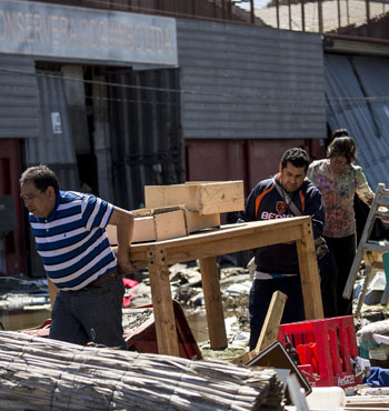 Residents carry furniture between debris caused by the sea in the port of Coquimbo.