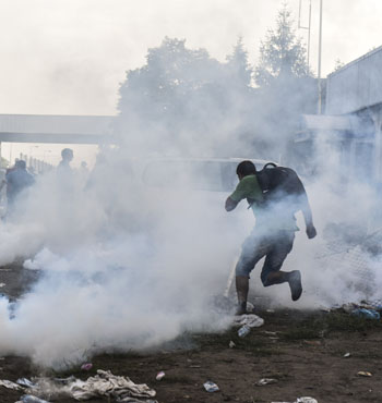 Migrants try to flee from the tear gas.