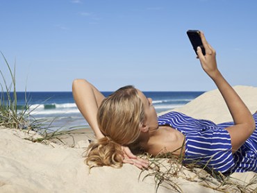 Woman lying in sand dunes texting.