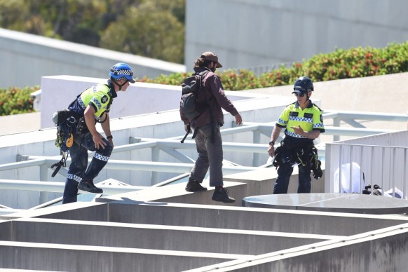 A police officer escorts a pro refugee protester who abseiled from the roof of Parliament House in Canberra.