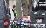 A blood-drenched man is wheeled out of the house.