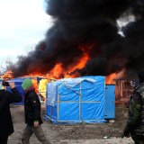 Migrants look on as a hut burns.