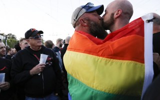 A couple shares a kiss as they embrace each other under a pride flag in the US.
