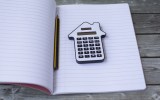 A house-shaped calculator, pencil and notebook.