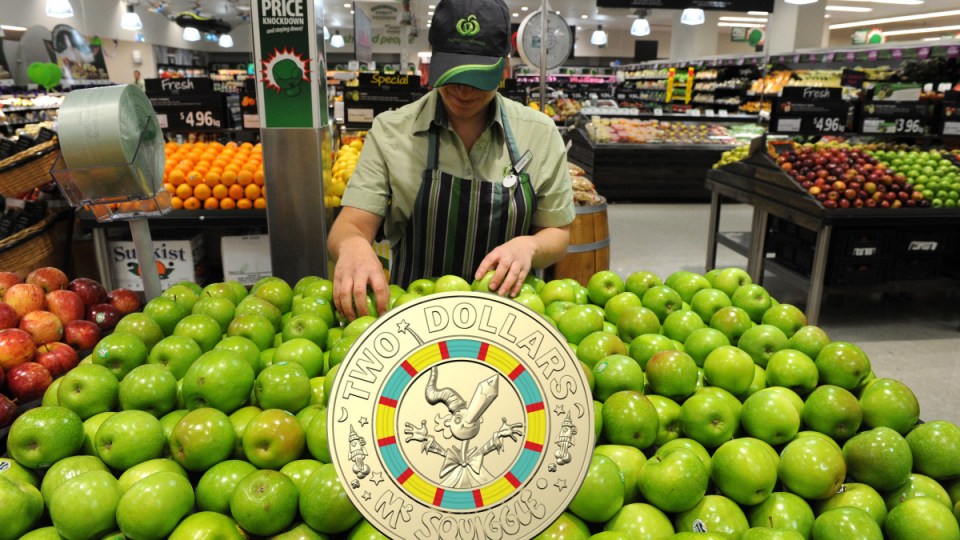 A Woolworths employee sorts apples with a coin superimposed on top.