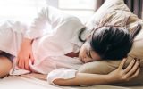 Woman Touching Abdomen In Pain While Sleeping On Bed At Home