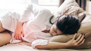 Woman Touching Abdomen In Pain While Sleeping On Bed At Home