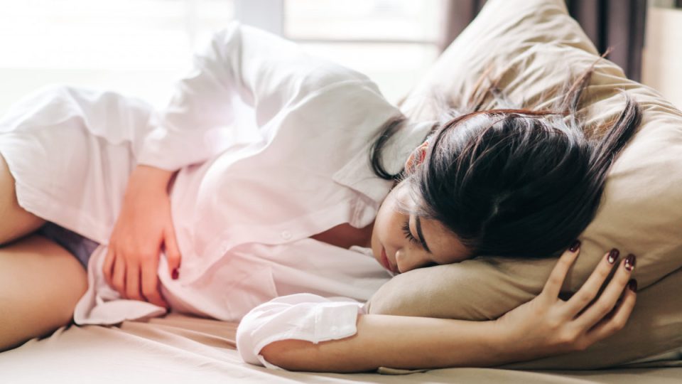 Woman Touching Abdomen In Pain While Sleeping On Bed At Home