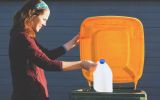 A woman placing a plastic milk bottle into a recycling bin