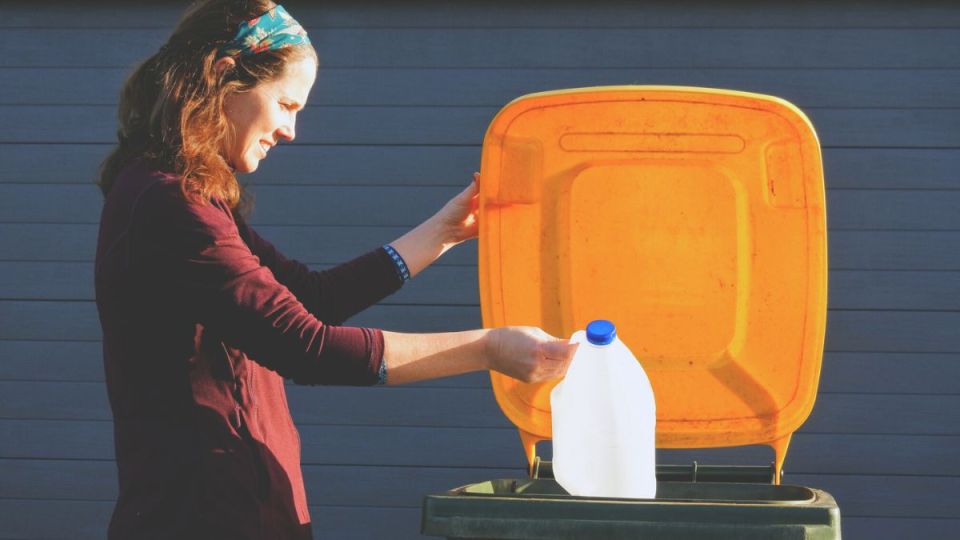 A woman placing a plastic milk bottle into a recycling bin