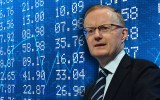Philip Lowe stands in front a screen of financial data.