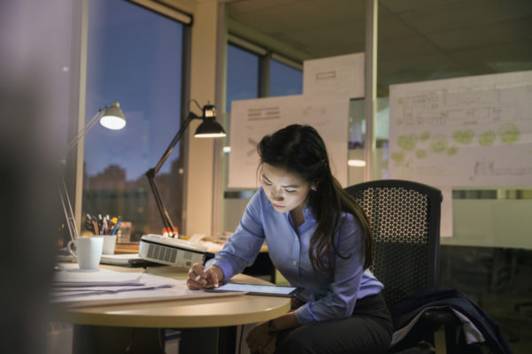 A woman works at her desk in an office late at night.