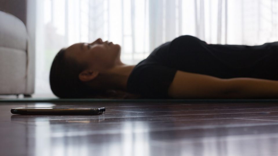 A person trying to relax while listening to guided meditation on her smartphone at home.