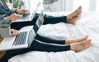 couple using laptops sitting in bed together
