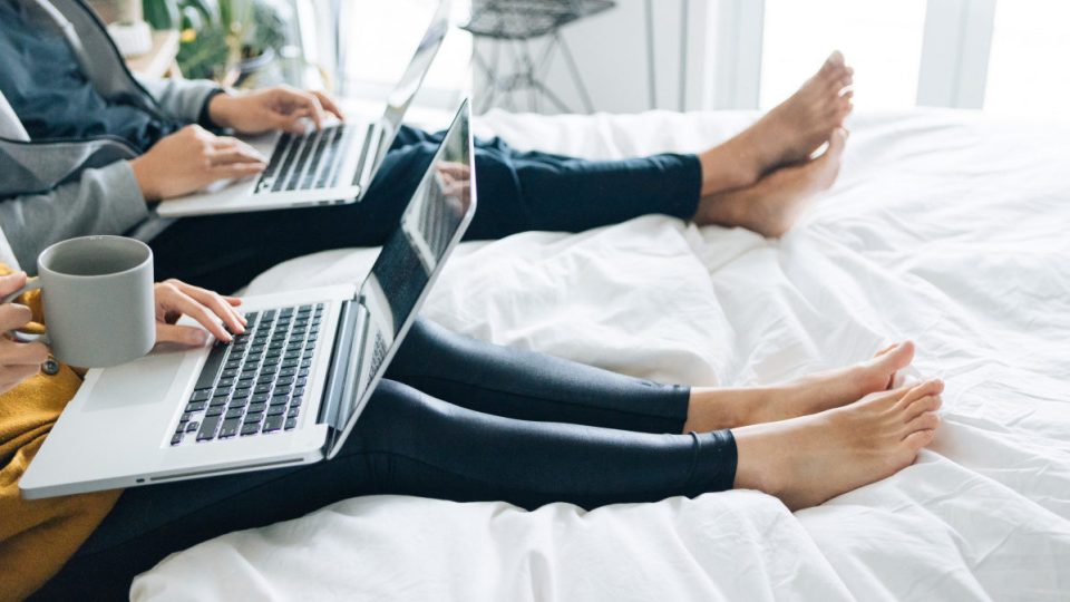 couple using laptops sitting in bed together