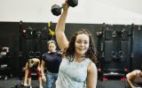 exercise Smiling woman doing one arm overhead dumbbell press during class in gym