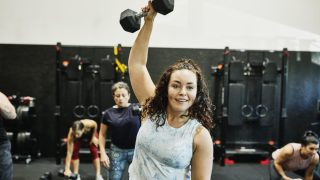 exercise Smiling woman doing one arm overhead dumbbell press during class in gym