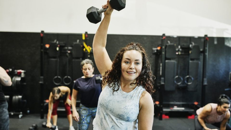 exercise Smiling woman doing one arm overhead dumbbell press during class in gym