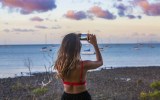 A girl takes a photo of the sunset over Airlie Beach Harbor