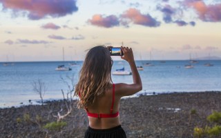 A girl takes a photo of the sunset over Airlie Beach Harbor