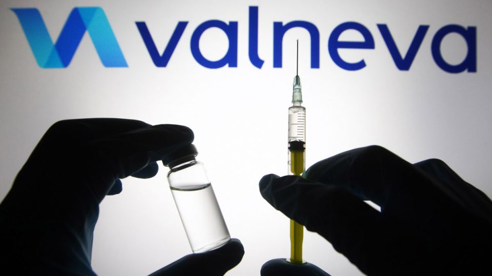 In this photo illustration, silhouette of hands in medical gloves hold a medical syringe and a vial in front of Valneva logo.