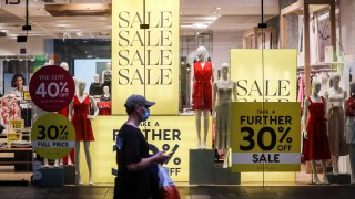 Pictured is a shopper walking past a shop displaying sales signs during the Boxing Day sales on December 26