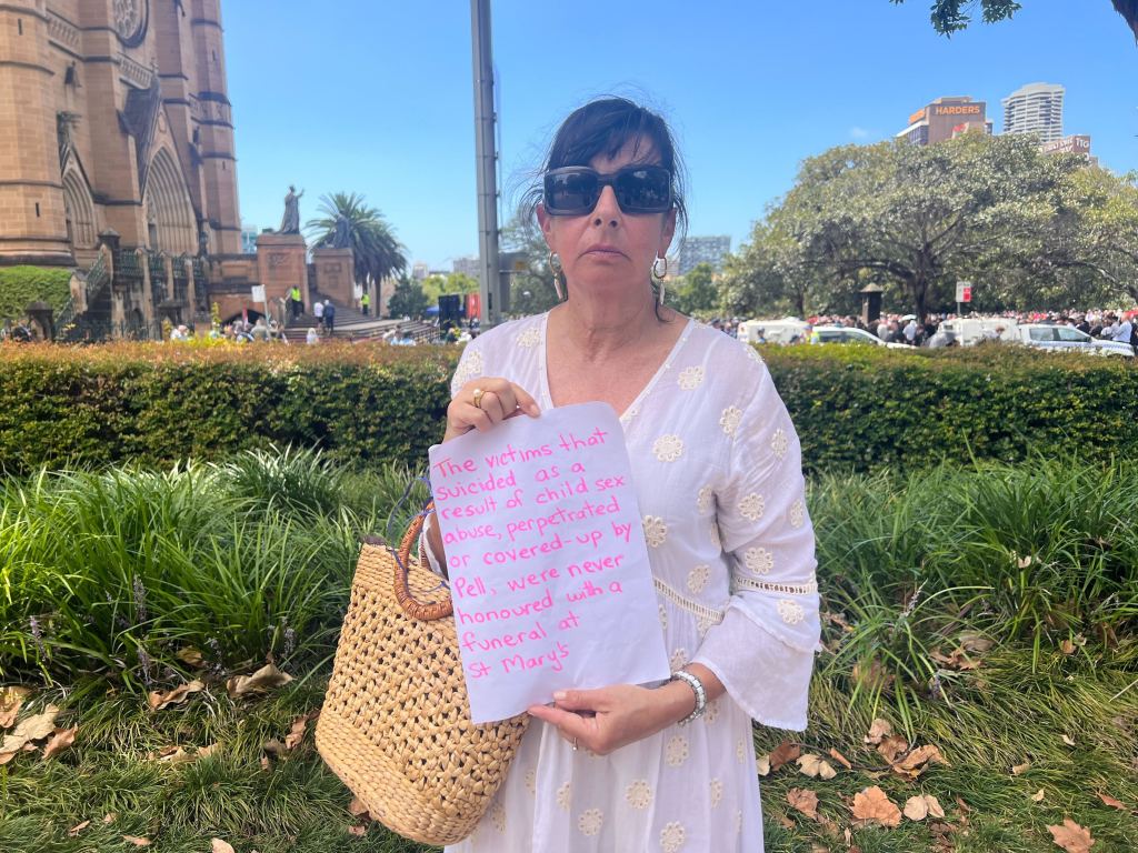 Pictured is a woman holding a sign outside of George Pell's funeral, saying victims of sexual assault within the church who died by suicide did not get a mass at a cathedral.