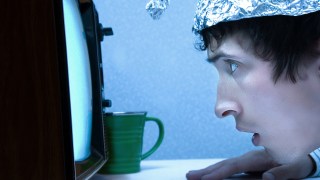 pictured is a man in a tin foil at to illustrate a conspiracy theory