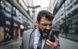 Young businessman walking outdoors in formalwear in downtown district, shouting at a mobile phone while recording a voice mail.