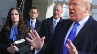 White House Press Secretary Stephanie Grisham (L) listens to U.S. President Donald Trump talk to reporters